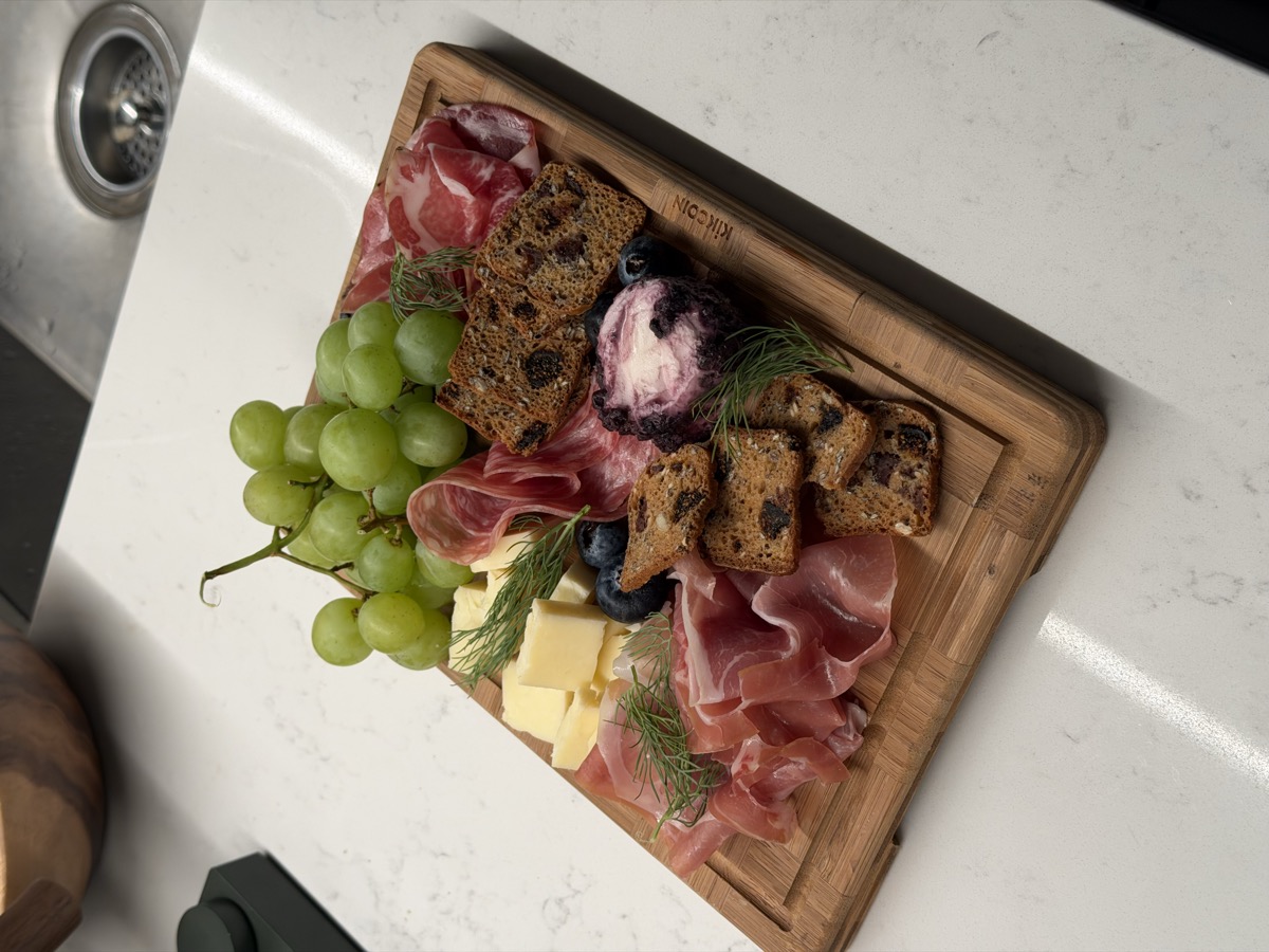 Charcuterie board with prosciutto, cheese, grapes, blueberries, dark bread, and fresh dill