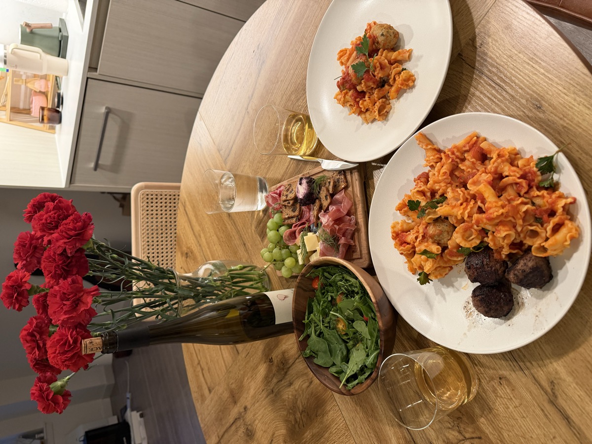 Dinner table with gigli pasta, meatballs, charcuterie board, arugula salad, and white wine