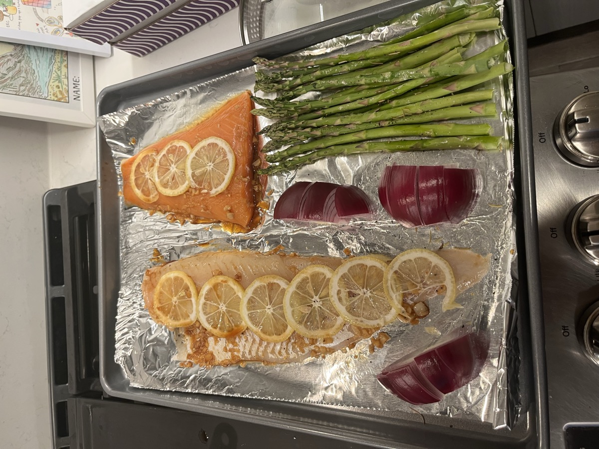 Sheet pan with salmon fillets topped with lemon slices, asparagus, and red onions before baking